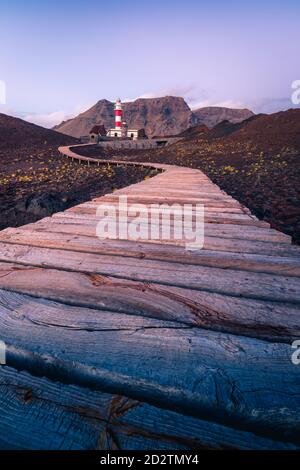 Kurvenreicher Pfad, der zum Leuchtturm führt, der sich auf einem Hügel in der Nähe des Meeres befindet Auf dem Hintergrund der Berge am Morgen in Teneriffa Stockfoto