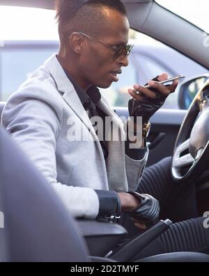 Seitenansicht eines ernsthaften ethnischen männlichen Unternehmers in edlem Anzug Mit Fliege fahren Luxus-Auto während des Gesprächs auf dem Smartphone Und wegschauen Stockfoto