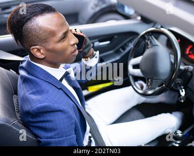 Von unten ernst ethnischen männlichen Unternehmer in edlem Anzug mit Bow tie Fahren Luxus-Auto beim Sprechen auf Smartphone und Wegschauen Stockfoto
