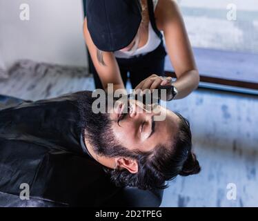 Von oben der Ernte unkenntlich weibliche Barbier mit Haarkamm In der Hand rasieren Bart des stilvollen brutalen Client mit Schnurrbart Im Friseurladen Stockfoto