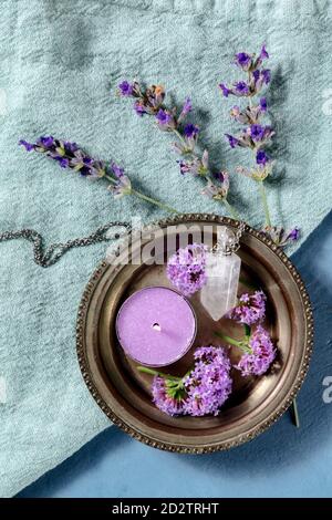 Botanische Präparate. Parfüm Fläschchen und Duftkerze, Lavendel und vervain Blumen, von oben auf einem blauen Hintergrund geschossen Stockfoto