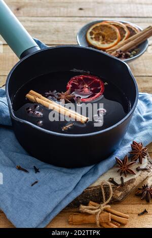 Hoher Winkel von Topf mit heißen leckeren Glühwein mit Zimtstange und getrocknete Orangen auf Tisch mit Stern angeordnet Anis und trockene Nelken in der Küche Stockfoto