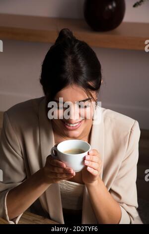 Von oben positiv träumerisch junge Hündin mit Tasse Aromatischer Kaffee, der am Tisch sitzt und beim Entspannen wegschaut Zu Hause Stockfoto