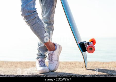 Unerkennbarer stylischer Skater in Jeans und Sneakers daneben Skateboard auf der Straße an sonnigen Tag im Sommer Stockfoto