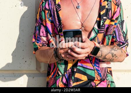 Crop-Ansicht von Hipster Mann an der Wand lehnte Chat auf Social Media via Handy an sonnigen Tagen Stockfoto