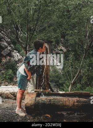 Ältere Frau am Frühling in der Natur. Ältere Frau, die Wasser aus der Quelle im Wald trinkt. Stockfoto