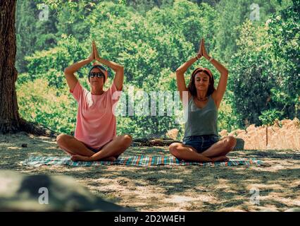 Zwei Frauen machen Yoga-Übungen in der Natur. Erwachsene sitzen in Lotusposition. Stockfoto