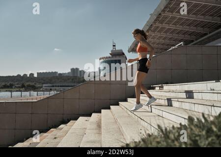 Seitenansicht der energiereichen, entschlossenen Sportlerin beim Sportswear Running Unten auf der Tribüne des Stadions während des Outdoor-Fitnesstrainings Stockfoto