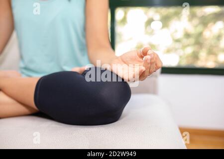 Crop flexible weibliche sitzende mit gekreuzten Beinen und Mudra Hände Auf dem Sofa und Yoga in Padmasana beim Üben von Achtsamkeit Mit geschlossenen Augen Stockfoto