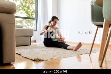 Friedliche Frau in Sportbekleidung Yoga in sitzenden vorwärts beugen üben Pose und Stretching Beine während auf Teppich im Leben sitzen Zimmer Stockfoto