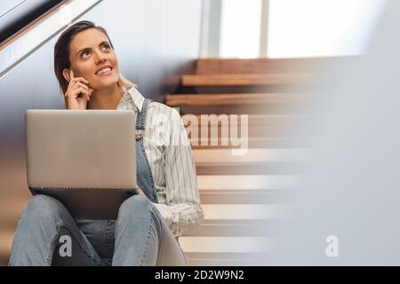 Freiberuflerin sitzt auf Holztreppe im modernen Gebäude und Arbeiten am Projekt während der Verwendung von Netbook Stockfoto