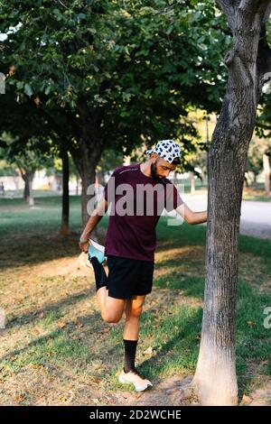 Konzentrierter männlicher Athlet in Sportswear, der beim Aufwärmen die Beine streckt Während des Trainings im Park Stockfoto