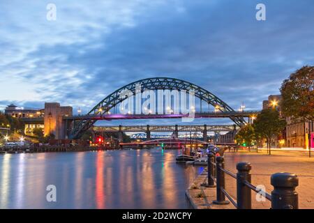 Blick auf den Fluss Tyne in der Abenddämmerung von Newcastles Kai in Richtung der ikonischen Tyne Bridge, Swing Bridge und High Level Bridge. Stockfoto