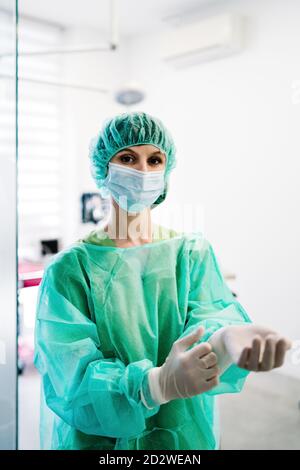 Ernsthafte weibliche Tierarzt Chirurg in Maske und Uniform setzen auf Schutzhandschuhe und Vorbereitung auf den Betrieb während des Stehens in Betrieb Theater der Tierklinik und Blick auf die Kamera Stockfoto