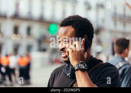 Lächelnder schwarzer Mann, der auf dem Handy mit ernstem Ausdruck spricht Die Straße Stockfoto