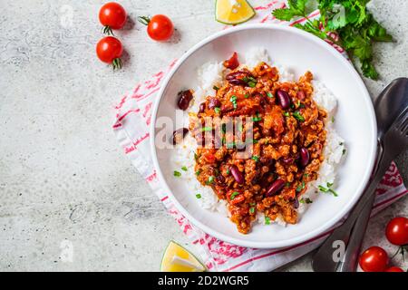 Chili con Carne mit Reis in einer weißen Schüssel. Rindereintopf mit Bohnen in Tomatensauce und Reis. Traditionelles mexikanisches Speisekonzept. Stockfoto