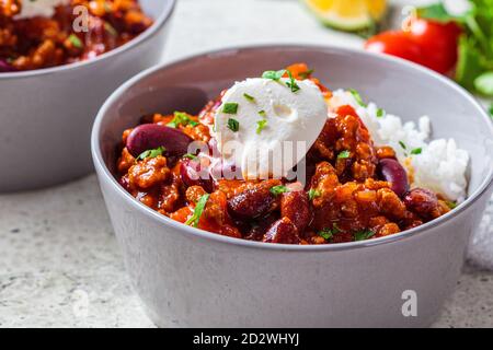 Chili con Carne mit Reis in einer grauen Schüssel. Rindereintopf mit Bohnen in Tomatensauce mit Sauerrahm und Reis. Traditionelles mexikanisches Speisekonzept. Stockfoto