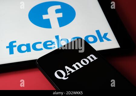 QAnon im Vergleich ZU FACEBOOK. QAnon-Unternehmenslogo auf dem Smartphone, das auf dem Tablet mit Facebook-Logos darauf platziert ist. Konzept für das Verbot von QAnon auf SoC Stockfoto