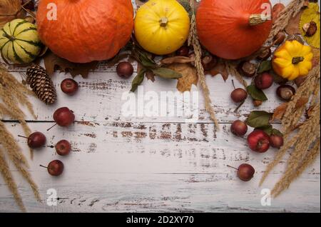 Herbstkomposition mit Kürbissen, Kastanien und gefallenen Blättern auf einem weißen Tisch. Stockfoto