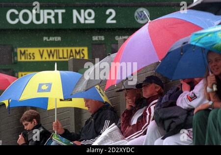 In dem, was sich zu einem vertrauten Anblick beim diesjährigen Turnier, Zuschauer sitzt unter ihrem Schirm, während sie warten, bis der Regen in Wimbledon heute Morgen (Donnerstag) stoppen. Das Wetter droht erneut, das Spiel des vierten Tages im All England Lawn Tennis Club ernsthaft zu verplagen. Foto von Neil Munns/PA. Stockfoto