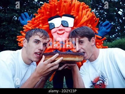 Die Neville-Brüder von Manchester United (Gary rechts und Bruder Phil links) lassen ihre Zähne in einen riesigen Jaffa-Kuchen sinken, gerade rechtzeitig, als sich das orangefarbene Tang-Monster in Bury, Lancs, heute (Donnerstag), anschleicht, um das orangefarbene Zentrum zu stehlen. Die Brüder sind Jaffa Kuchen Liebhaber und essen sie als Teil einer energiereichen, fettarme Fußballer Ernährung. Pic Dave Kendall. Stockfoto