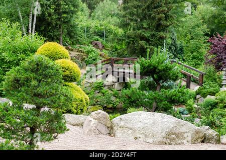 Blick auf den japanischen Garten mit geformten Bäumen, Steinen, Sand, Holzbrücke. Polen, Shklarska poreba. Selektiver Fokus. Stockfoto