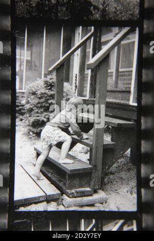 Feine 70er Jahre Vintage Schwarz-Weiß-Fotografie eines kleinen Mädchens, das die vordere Treppe hinauf und hinunter klettert. Stockfoto