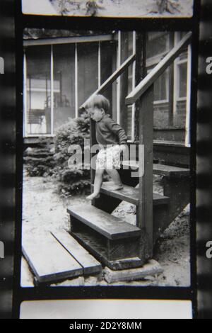 Feine 70er Jahre Vintage Schwarz-Weiß-Fotografie eines kleinen Mädchens, das die vordere Treppe hinauf und hinunter klettert. Stockfoto