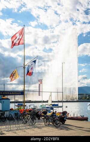 Die Schweizer Flagge fliegt an einem stürmischen Tag am Ufer des Genfersees in Genf, Schweiz, mit dem Jet d'Eau Wasserstrahlbrunnen in der Ferne Stockfoto