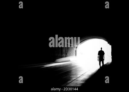 Verschwommenes Bild einer menschlichen Silhouette in einem Tunnel. Ein Mann, der ins helle Licht in Unschärfe geht. Stockfoto