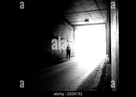 Verschwommenes Bild einer menschlichen Silhouette in einem Tunnel. Ein Mann, der ins helle Licht in Unschärfe geht. Stockfoto