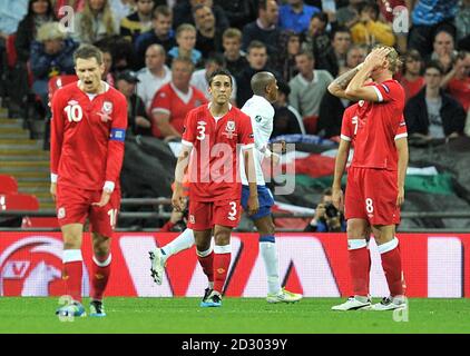 Wales' Aaron Ramsey (links) und Neil Taylor (Mitte) stehen niedergeschlagen, als Englands Ashley Young (hinten) das Eröffnungstreffer seiner Mannschaft während des UEFA Euro 2012 Qualifying-Spiels im Wembley Stadium, London feiert. Stockfoto