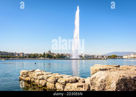 Die Stadt und die Bucht von Genf, Schweiz, mit ihrem Wasserstrahlbrunnen auf dem Genfer See, von einem Steinsteg aus gesehen von einem sonnigen Sommermorgen. Stockfoto