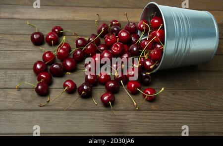 Frische rote reife Kirschen in einem kleinen Metalleimer umgedreht Auf dem Holztisch Stockfoto