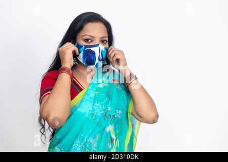 Portrait einer Inderin im traditionellen indischen Sareehand, mit Covid 19 Schutzmaske und steht gegen weiße Wand, Studioportrait, Stockfoto