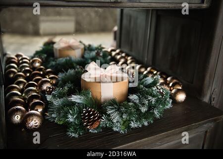 Runde Handwerk Geschenkbox mit rosa Band, Bogen, steht auf einem Holztisch in einem Nadelbaum Lichter Girlande, Scheibe von Weihnachtsbaum goldenen Kugeln. Kopieren Raum Stockfoto