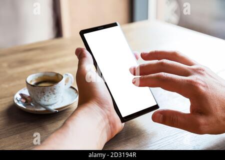 Nahaufnahme der Hände des Mannes mit Handy-Smartphone mit leerem Kopierraum Bildschirm. Bild des Mannes, der an einem Tisch mit einem Kaffee im Café sitzt und mobil benutzt Stockfoto