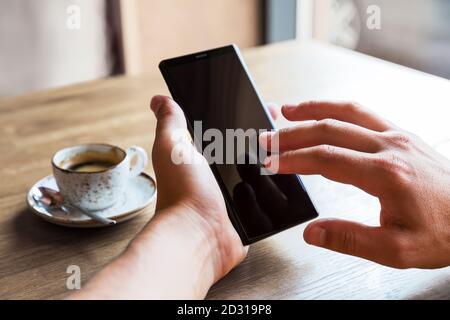 Nahaufnahme der Hände des Mannes mit Handy-Smartphone mit leerem Kopierraum Bildschirm. Bild des Mannes, der an einem Tisch mit einem Kaffee im Café sitzt und mobil benutzt Stockfoto