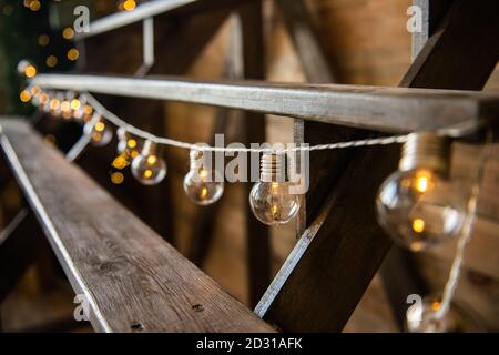 Weihnachtsgirlande von Glühbirnen, die von einer Holztreppe hängen. Festliche Heimtextilien. Skandinavischer Loft-Stil.Textur Hintergrund, Kopierraum Stockfoto