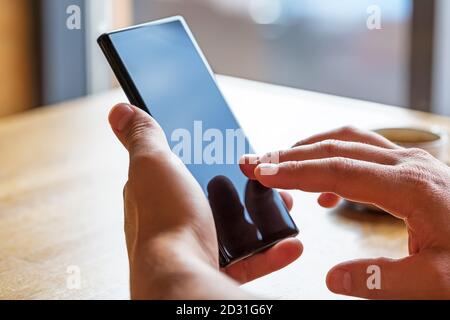 Nahaufnahme der Hände des Mannes mit Handy-Smartphone mit leerem Kopierraum Bildschirm. Bild des Mannes, der an einem Tisch mit einem Kaffee im Café sitzt und mobil benutzt Stockfoto