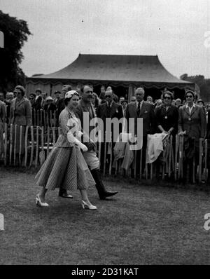 Die Königin, im sommerlichen gepunkteten Outfit, gekrönt von einem eng anliegenden Hut, geht mit Lord Cowdray zum königlichen Gehege, um das Finale des Krönungscups zwischen den Polo-Teams Argentiniens und Englands im Cowdray Park, Sussex, zu beobachten. Stockfoto