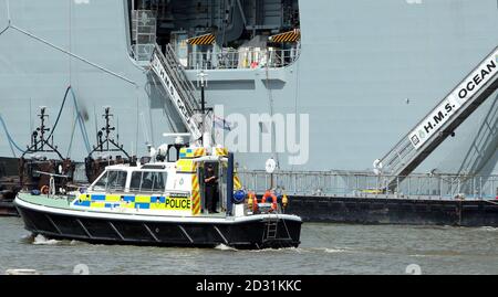 Ein Polizeiboot passiert das Royal Navy-Schiff HMS Ocean, das an der Themse in Greenwich als Teil der Armed Forces Security für die Olympischen Spiele 2012 in London festgemacht ist. Stockfoto