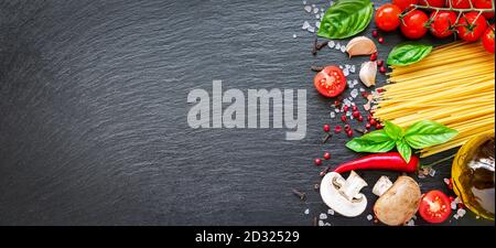 Lebensmittelzutaten auf dunklem Hintergrund. Tomaten, Spaghetti, Gewürze, Knoblauch und Basilikumblätter auf schwarzem Hintergrund. Italienisches Essen, Gesundheit oder Kochkonzept Stockfoto