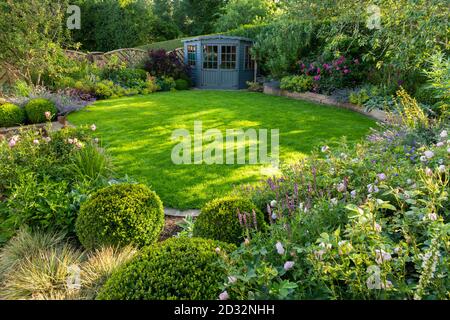 Landschaftlich schöner sonniger privater Garten (modernes Design, Sommerblumen, Randpflanzen, Sträucher, Sommerhaus Schuppen, niedrige Mauer, Rasen) - Yorkshire, England Stockfoto