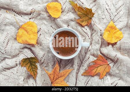 Eine Tasse frischen Kaffee auf gestricktem karierten, gelben Herbstblättern. Konzept für Herbstferien. Draufsicht, flach liegend. Stockfoto