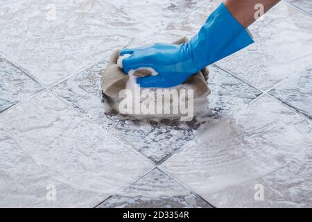 Hand des Mannes trägt blaue Gummihandschuhe ist mit einem Schwamm Reinigung der Fliesenboden. Stockfoto