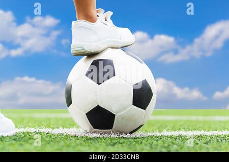 Füße eines Jungen in weißen Sneakers, der mitten auf dem Fußballfeld auf einen Fußball tritt. Stockfoto