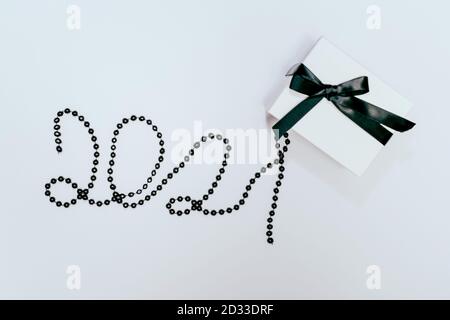 Weiße Geschenk- oder Geschenkbox mit schwarzem Band und 2021 Nummer aus Perlen auf weißem Hintergrund. Flache Lay-Komposition für Geburtstag, Weihnachten, Hochzeit. Freier Speicherplatz für Text. Stockfoto