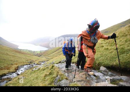 Der langjährige Fundraiser Lloyd Scott, der versucht, die Three Peaks zu besteigen, während er einen Tiefseetauchanzug trägt, wird von Mitgliedern seines Support-Teams während seiner Challenge auf Scafell Pike im Lake District National Park in Cumbria begleitet. Stockfoto