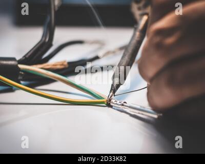 Elektriker verwenden einen Lötkolben, um die Drähte mit dem Metallstift mit Lötkabel zu verbinden. Stockfoto